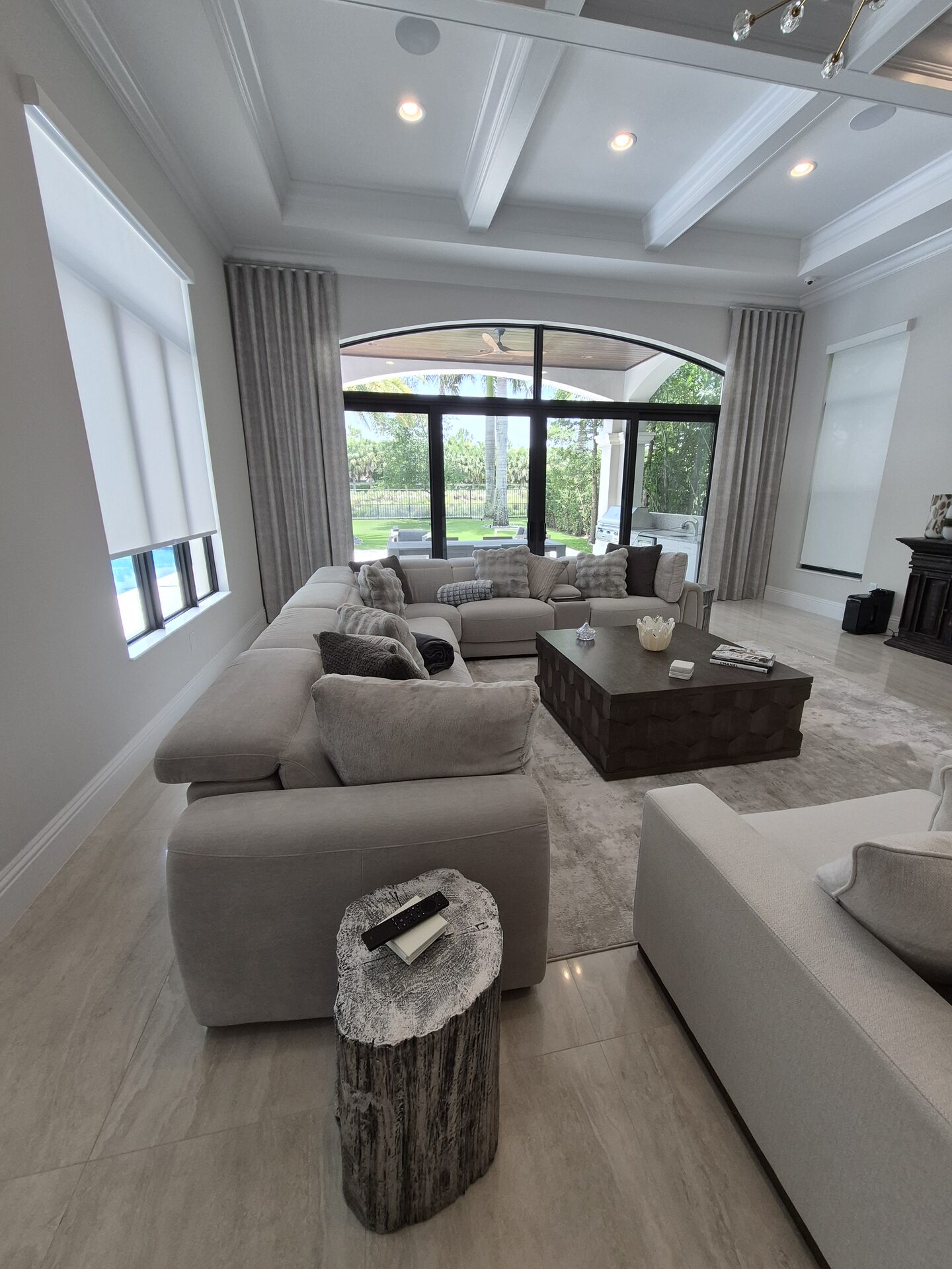 Motorized solar roller shades lowered over a wall of glass facing a pool, South Florida estate