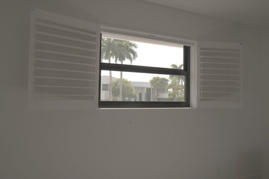Guest house window with lacquered basswood shutter panels swung open and palm trees outside, Boca Raton