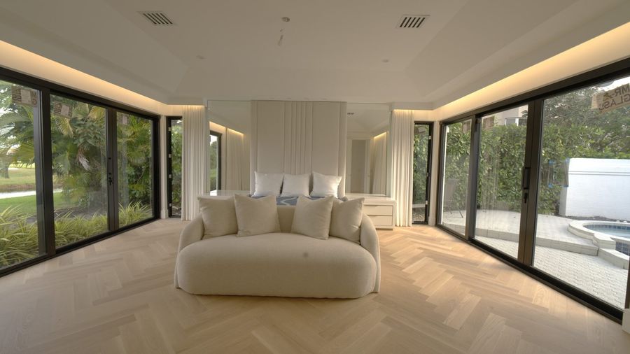 Master bedroom with Kravet Smart ripplefold drapery stacked open under a custom wood valance, glass walls to the garden, Boca Raton