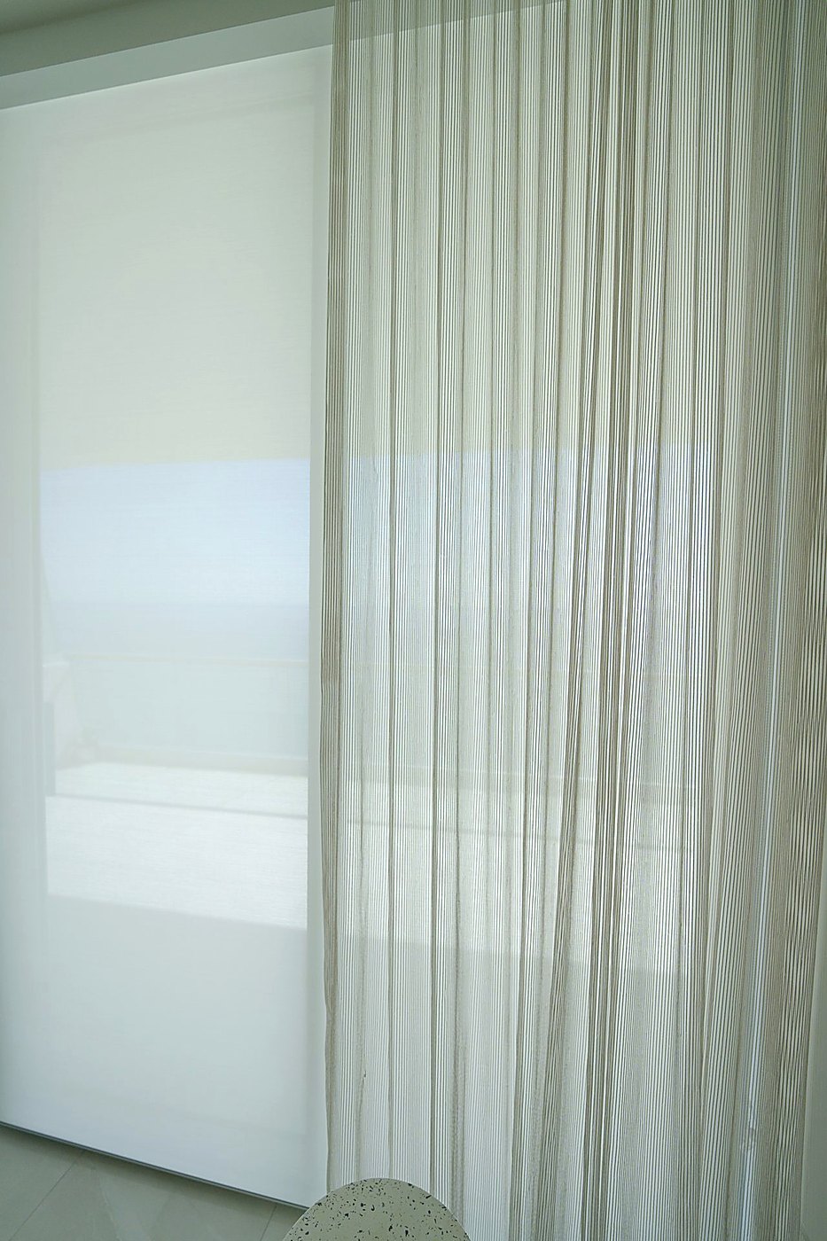 Close up of a Romo Zyla Porcelain sheer in front of a solar shade, showing the weave and the finished edge of the shade