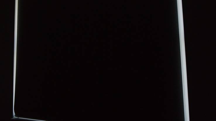 The bedroom with the blackout fully down, only a thin halo of light at the window edge