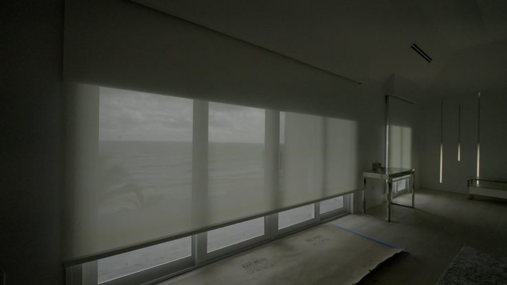 Luna White Lutron blackout shade rolling up off a wall of ocean glass