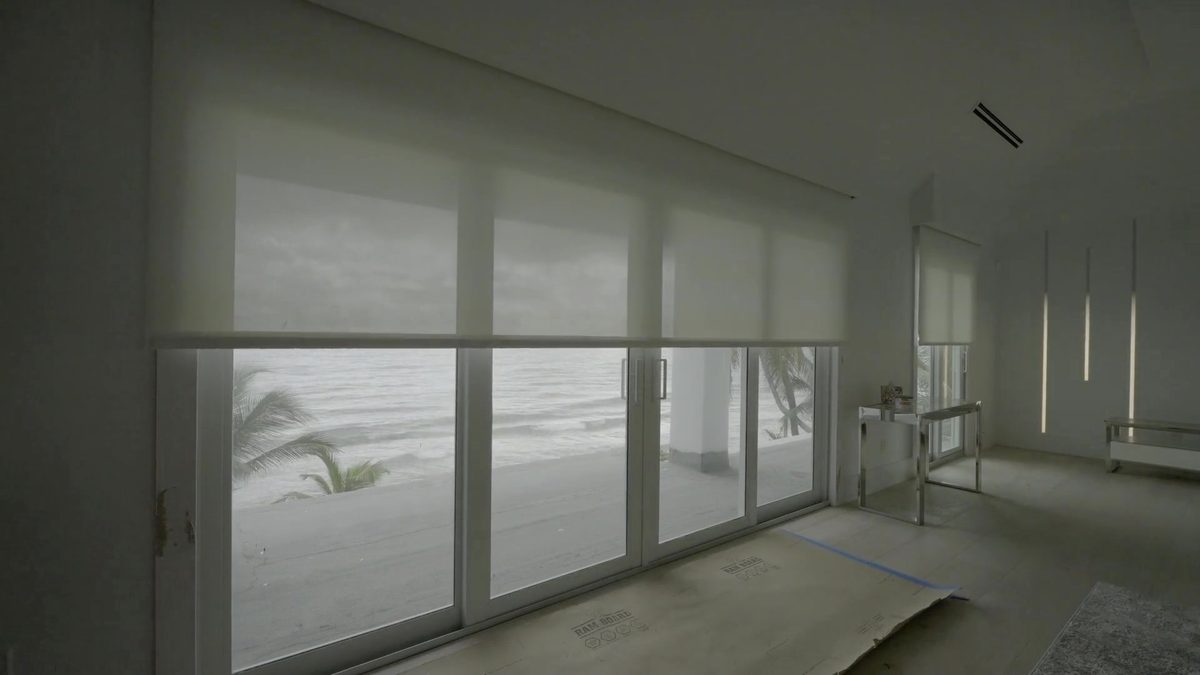 Solar screen rising to reveal the ocean and palms through the sliding glass wall, Hillsboro Beach