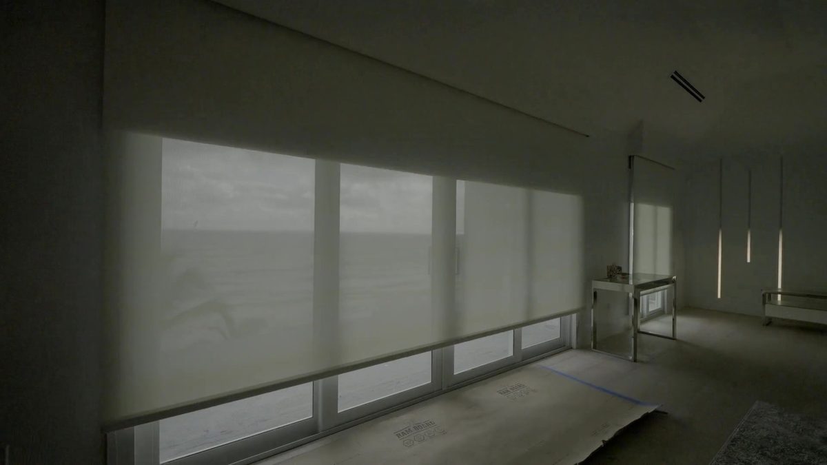 Primary bedroom with the solar screen layer of the dual shade lowered over a wall of ocean glass, Hillsboro Beach