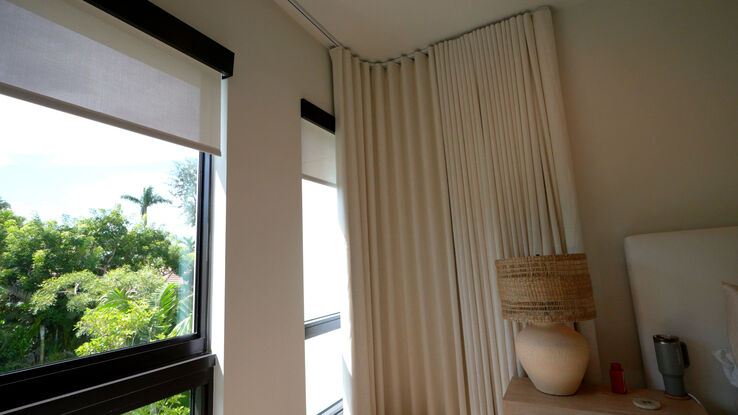 Close-up of the curved drapery track turning the corner above a Lutron roller shade with black architectural fascia