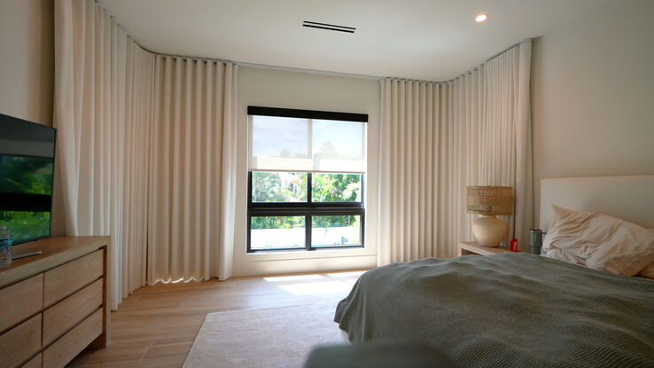 Blackout drapery closing around a bent motorized track over three angled master bedroom windows in Boca Raton