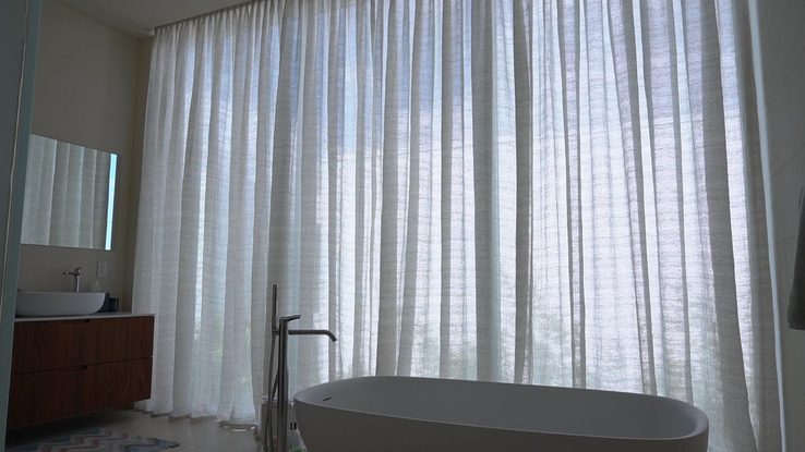 Primary bathroom with a freestanding tub against floor-to-ceiling sheer draperies