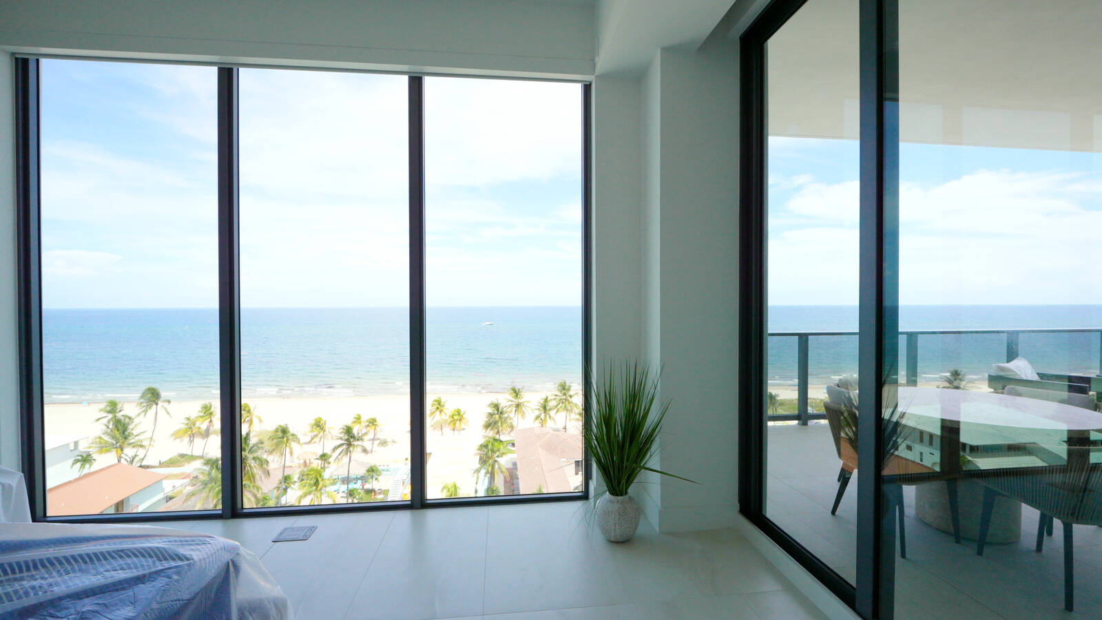 Floor-to-ceiling corner glass in an oceanfront bedroom with the roller shades raised, the beach and the ocean in view, Salato, Pompano Beach