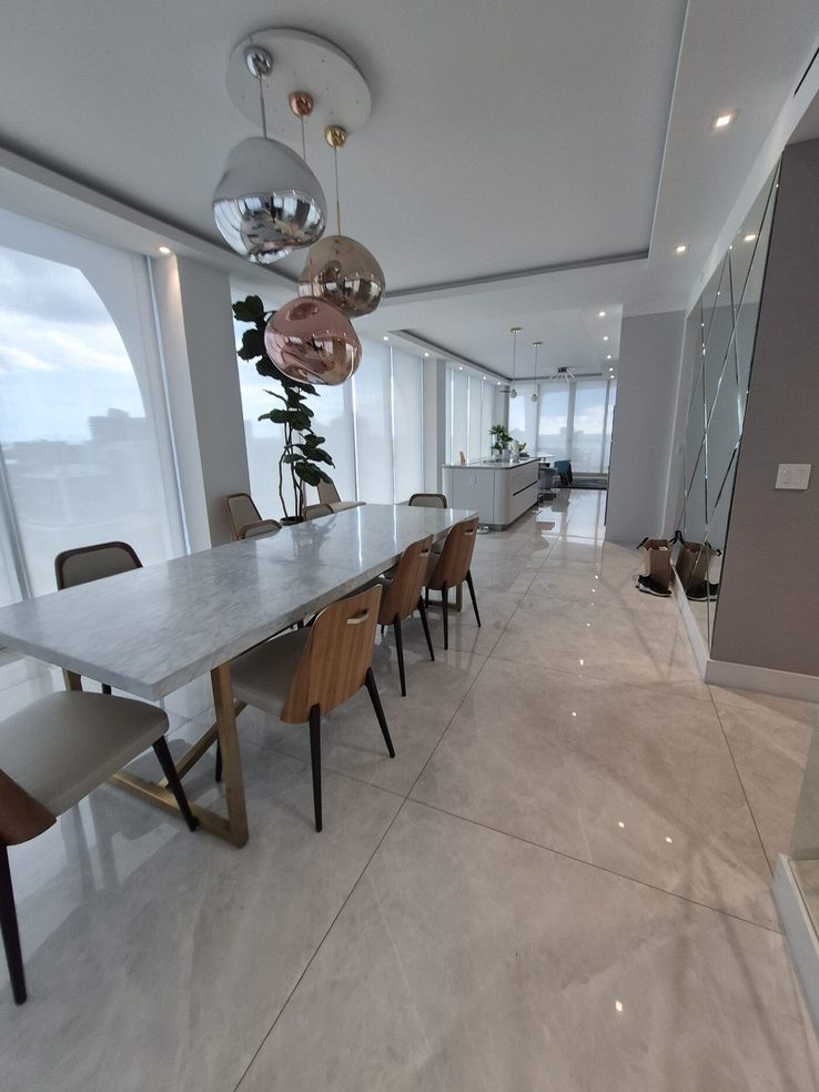 Dining table under the arched corner bay with the kitchen beyond, shades recessed into the ceiling