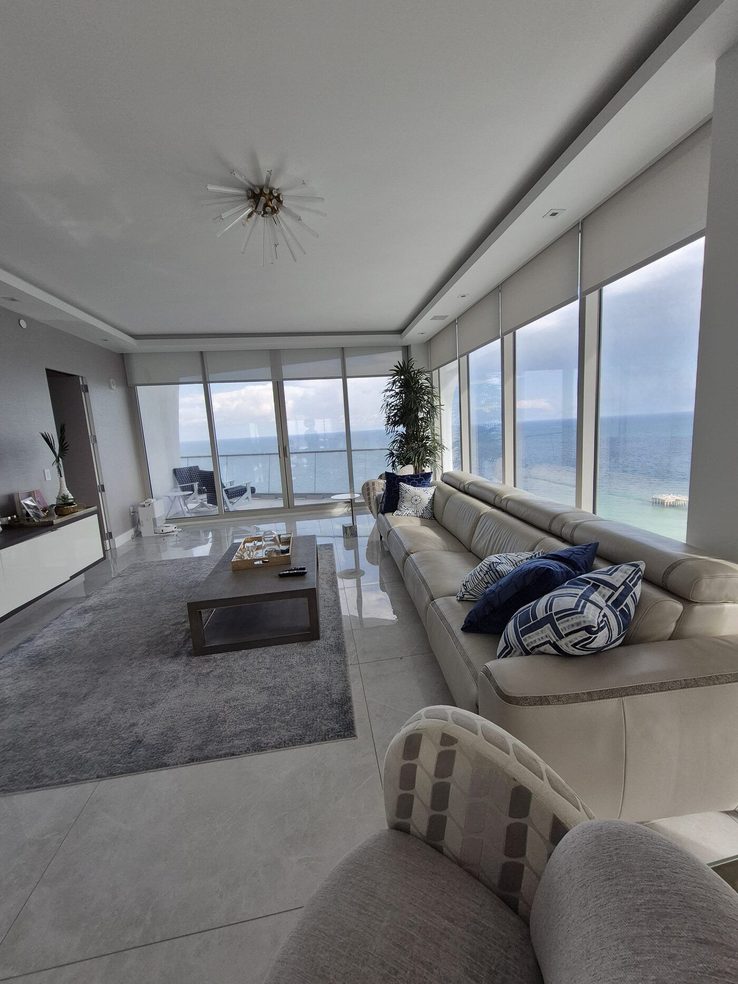 Great room with recessed Crestron solar shades along the oceanfront glass in Sunny Isles Beach